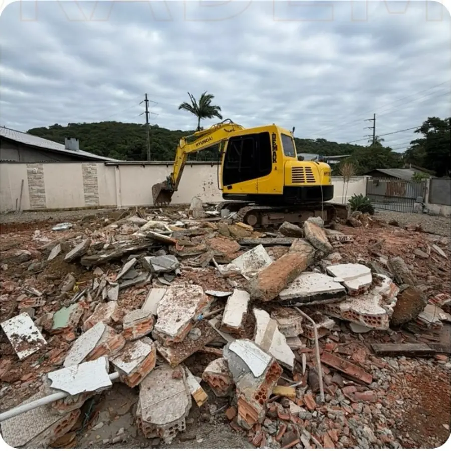 Terreno com entulho e escavadeira da Demak iniciando a limpeza